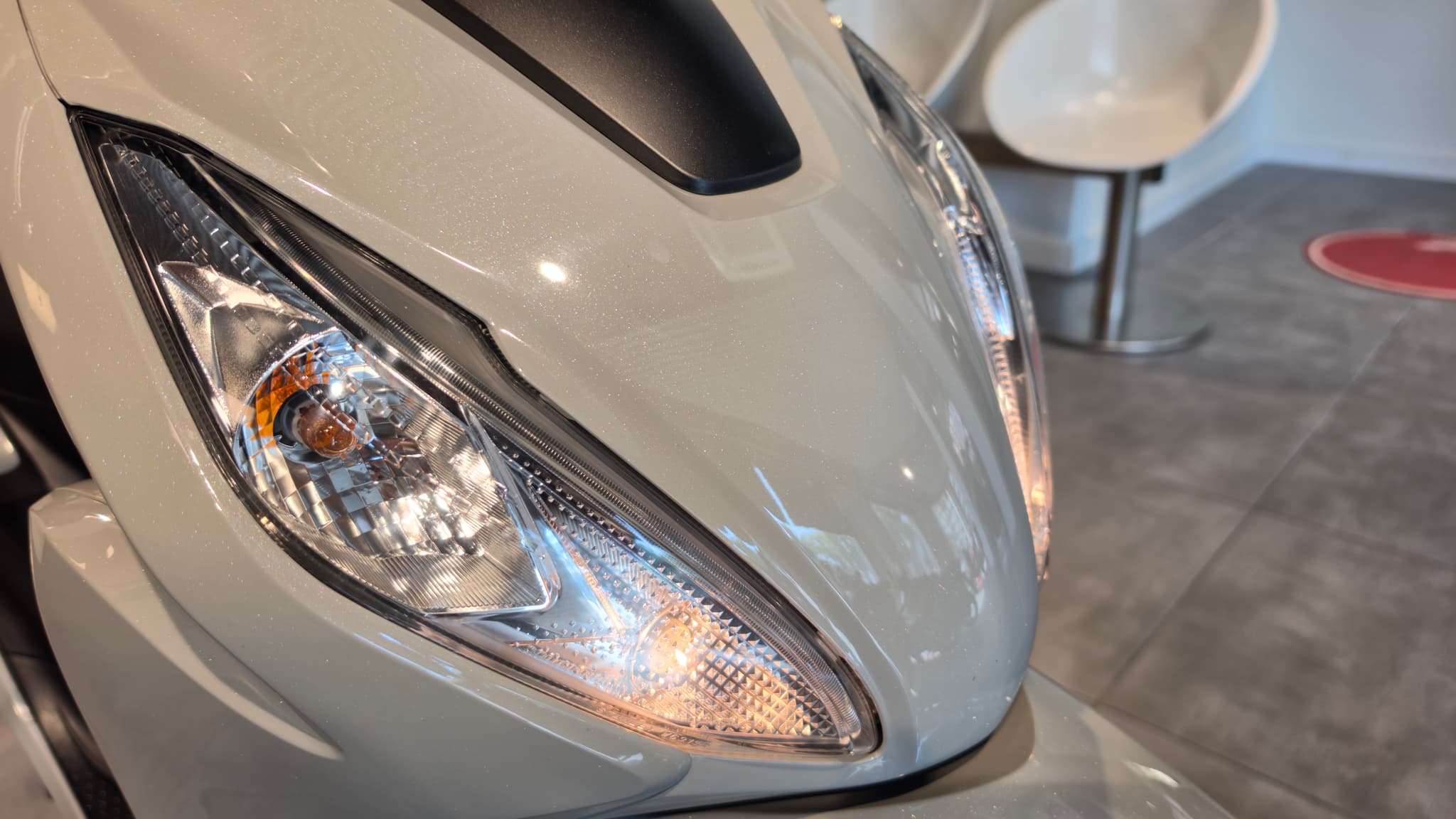 Detalle del faro delantero de una moto Honda Vision 110 de color blanco perla.