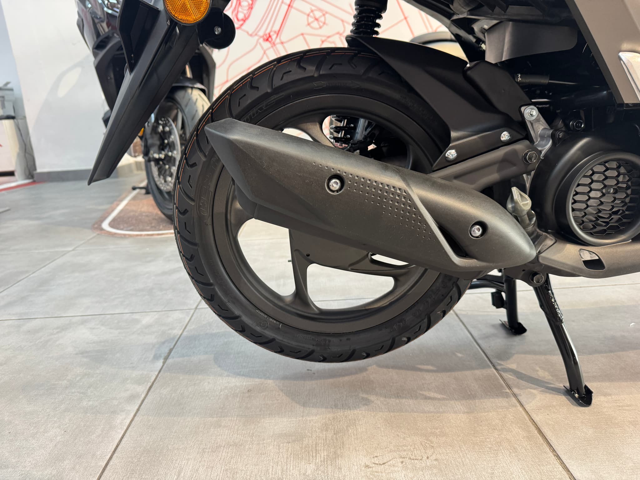 Detalle de la rueda trasera y escape de Honda Vision 110 marrón mate