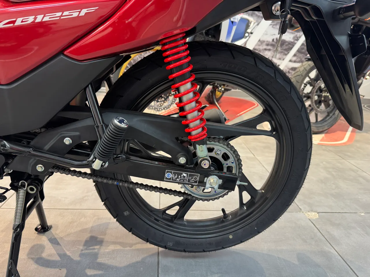 Detalle de la rueda trasera y suspensión de una Honda CB125F roja.