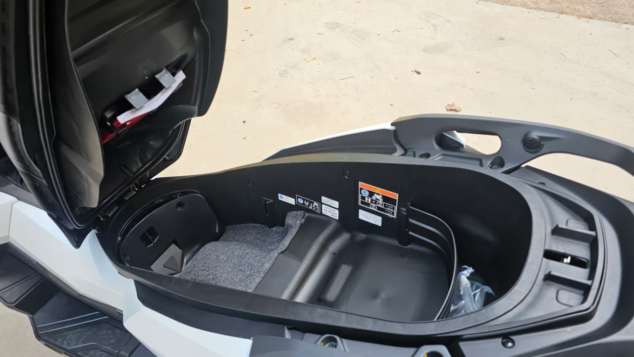 Compartimento de almacenamiento bajo el asiento de una Honda ADV 350 blanca abierto y vacío