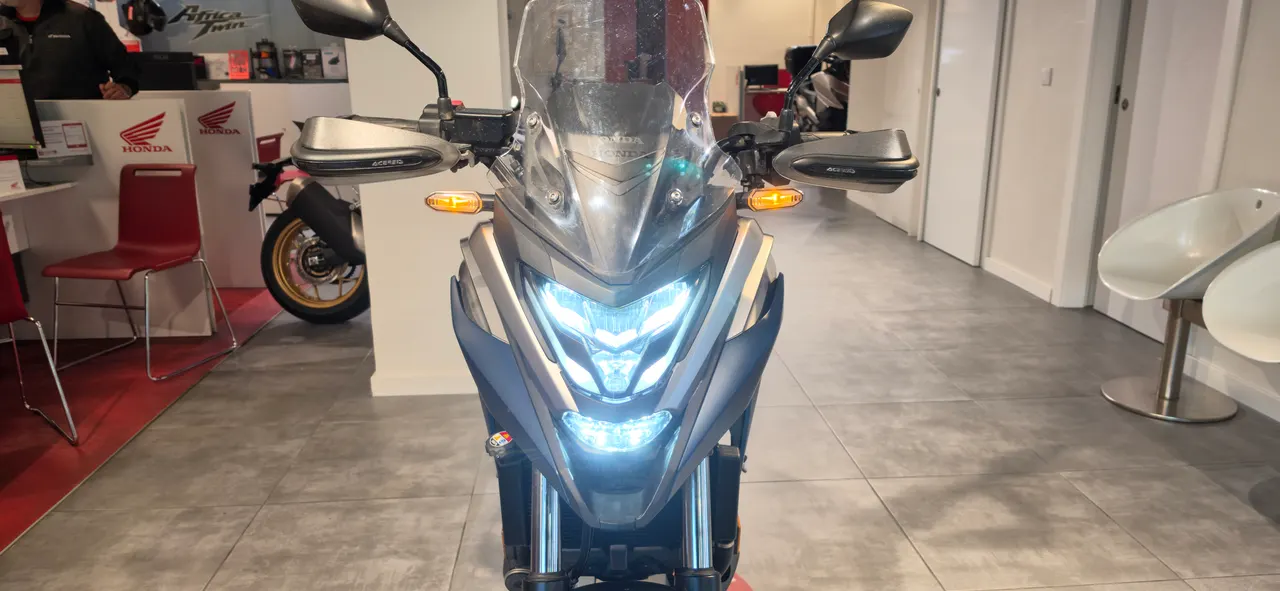 Vista frontal de una moto Honda NC750X con luces encendidas en un concesionario.