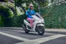 Mujer con casco rosa conduciendo una scooter Honda PCX 125 blanca en una calle arbolada