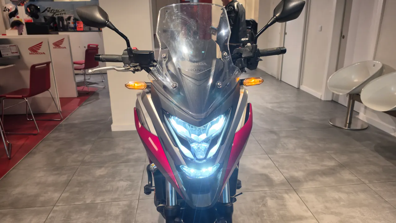 Vista frontal de una moto Honda NC750X de color rojo y gris con luces LED encendidas.