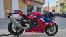 Moto deportiva Honda CBR1000RR-R Fireblade SP roja, blanca y azul estacionada frente a un concesionario Honda.