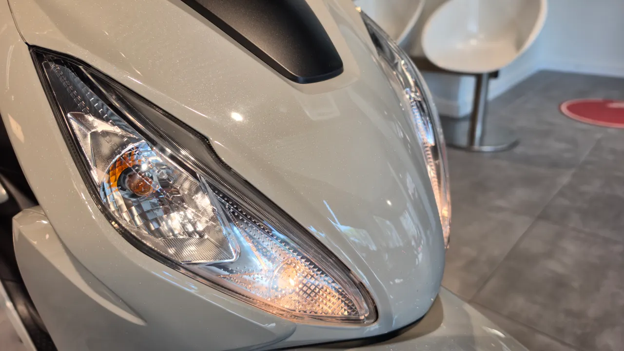 Detalle del faro delantero de una moto Honda Vision 110 de color blanco perla.