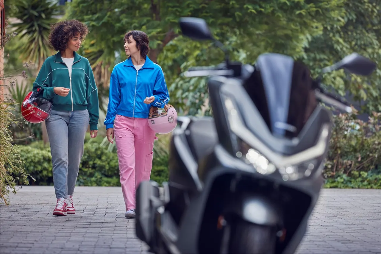 Honda PCX 125 negra en primer plano con dos mujeres caminando y cascos