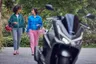 Honda PCX 125 negra en primer plano con dos mujeres caminando y cascos