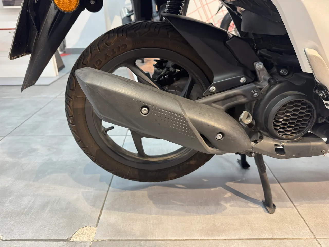Detalle de la rueda trasera y el sistema de escape de una moto Honda Vision blanca.