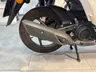 Detalle de la rueda trasera y el sistema de escape de una moto Honda Vision blanca.