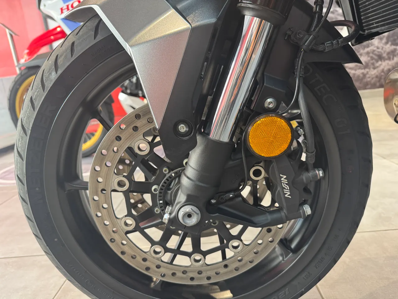 Primer plano de la rueda delantera de una motocicleta, mostrando el disco de freno, la pinza Nissin y la horquilla delantera.