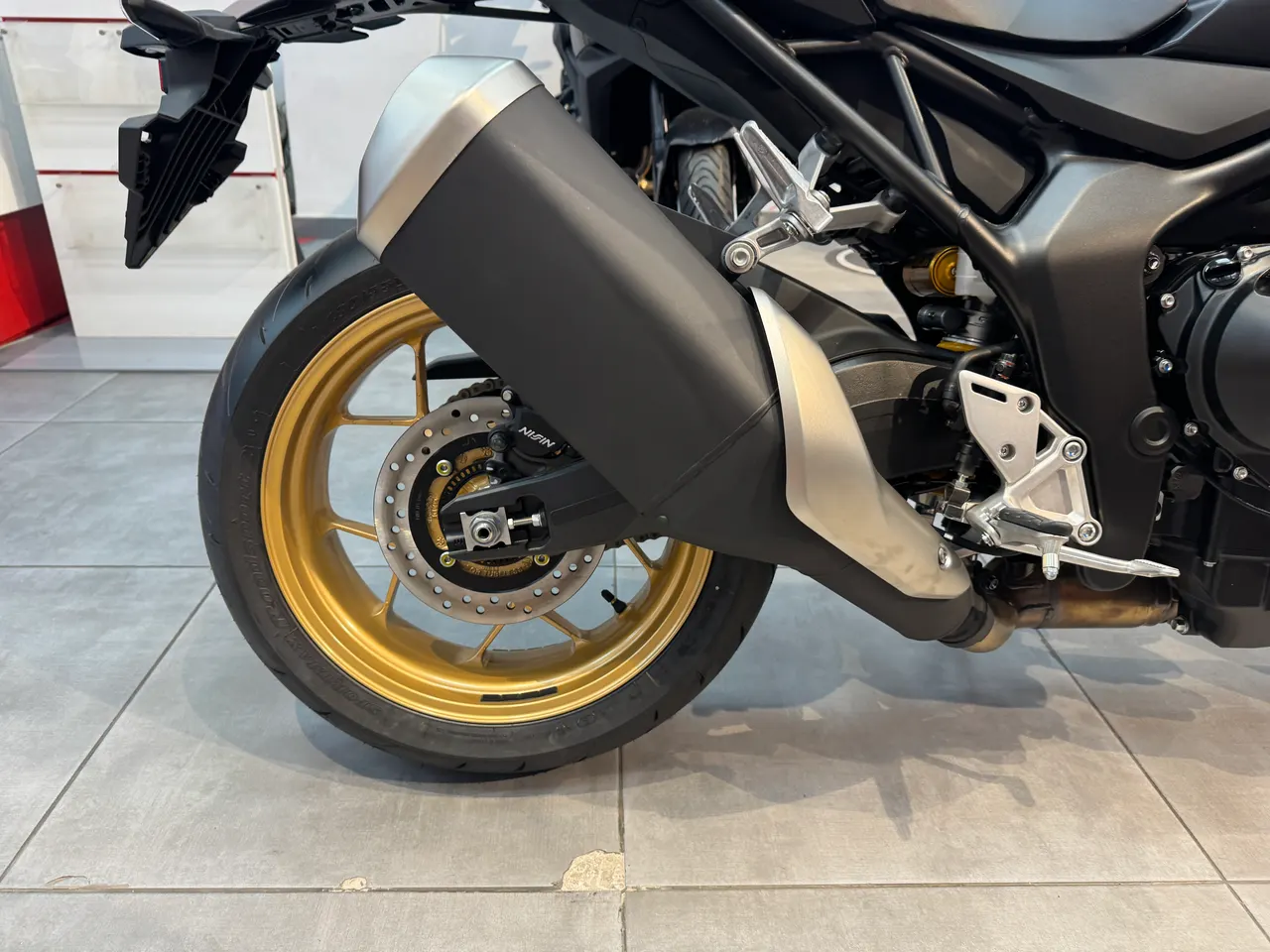 Detalle de la rueda trasera dorada y el escape negro de una Honda Hornet 1000 SP.