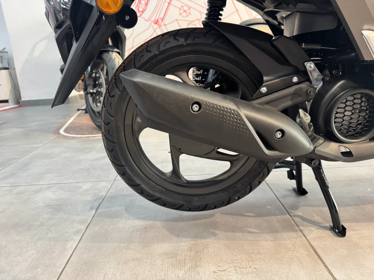 Detalle de la rueda trasera y escape de Honda Vision 110 marrón mate