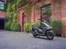 Scooter Honda PCX 125 gris oscuro aparcado frente a una pared de ladrillo con plantas