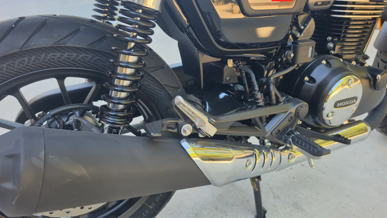 Detalle de la rueda trasera, amortiguador y escape de una Honda GB350S azul.